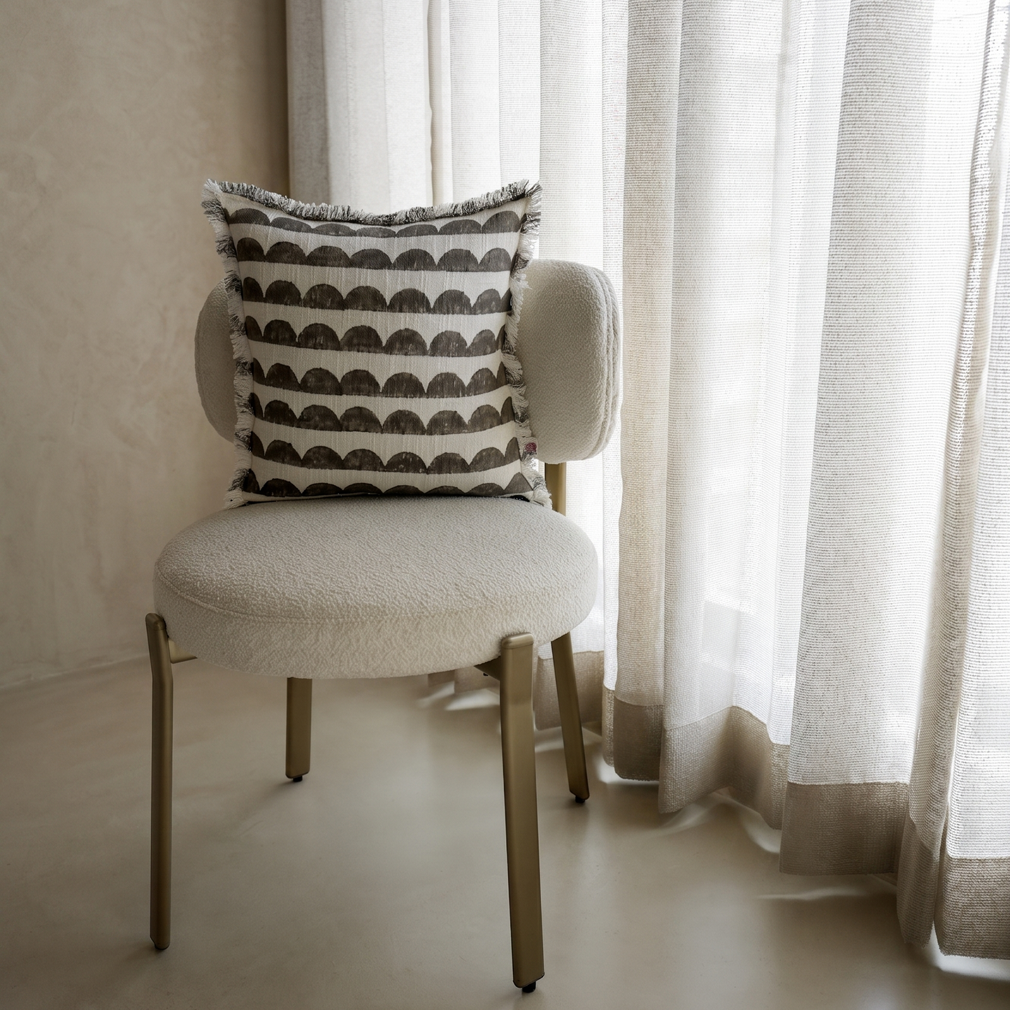 Chair with a patterned pillow in front of sheer curtains