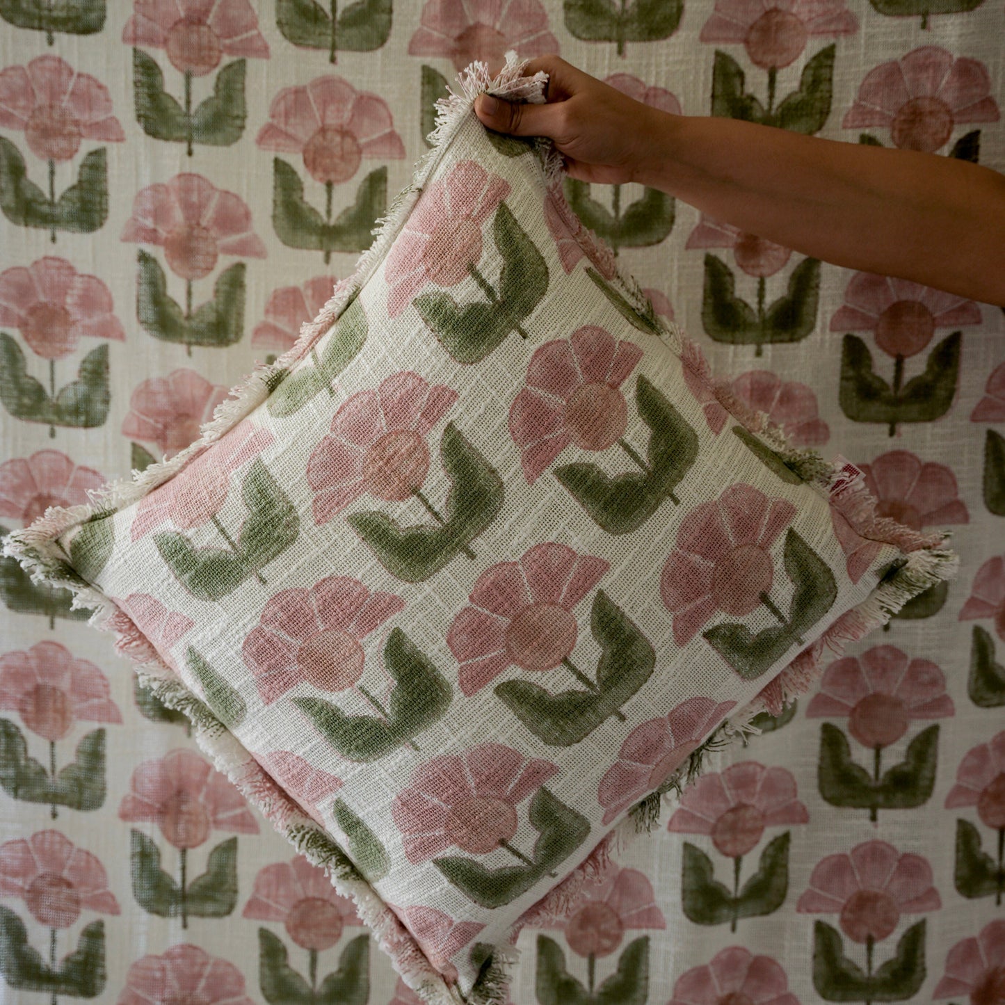 Floral patterned fabric with a hand holding a folded piece of fabric.