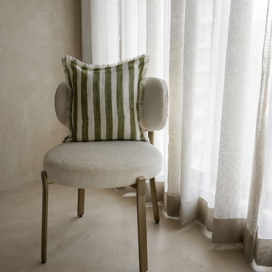 Chair with a striped pillow in front of sheer curtains