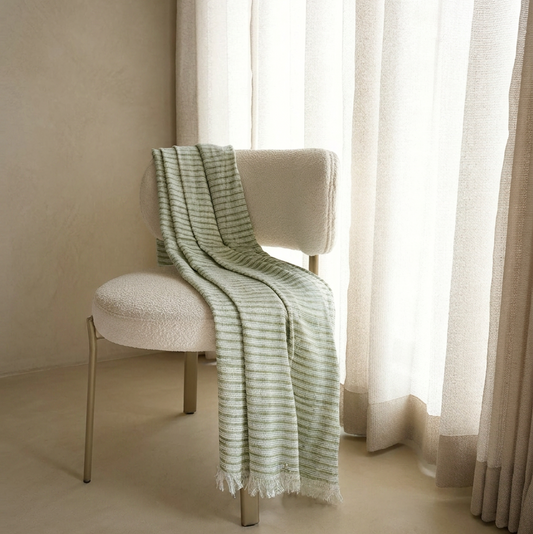 Chair with a green and white striped cover in a room with light-colored walls and a window.