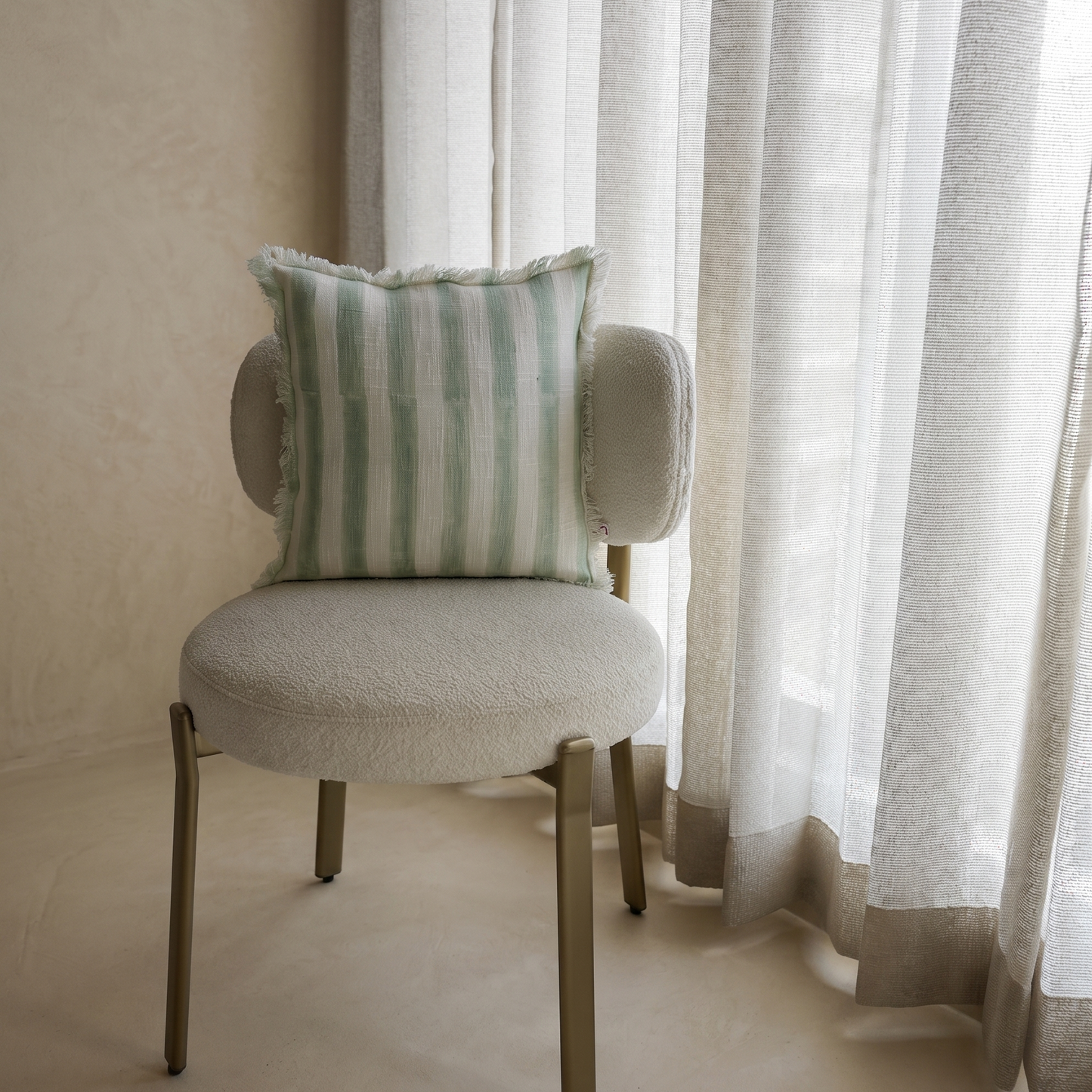 Chair with a striped pillow in front of sheer curtains