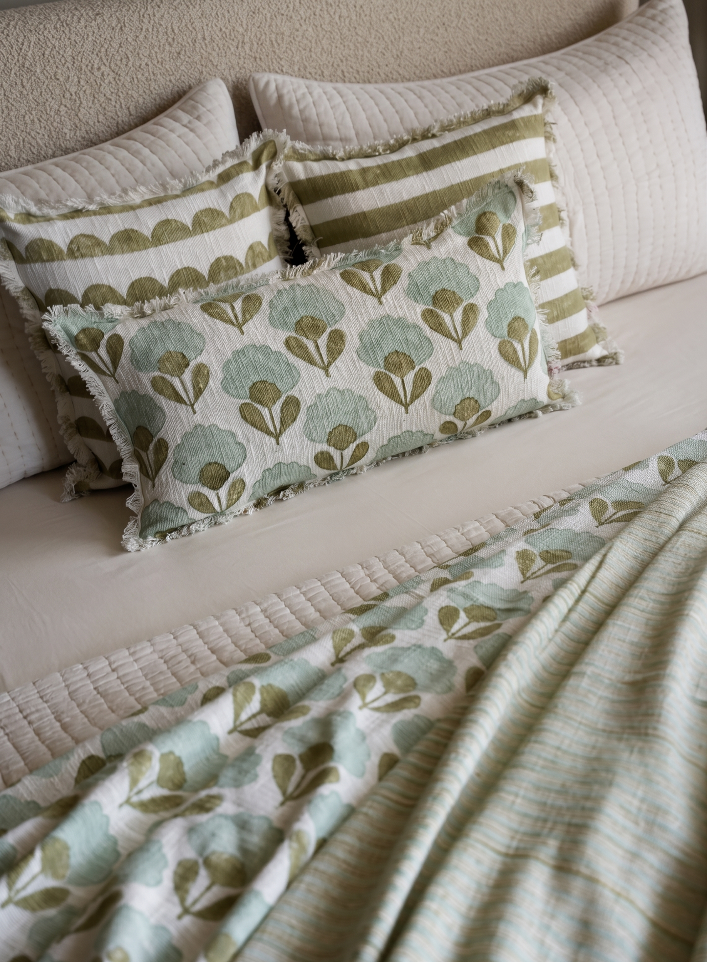 Bed with patterned green and beige bedding and pillows.