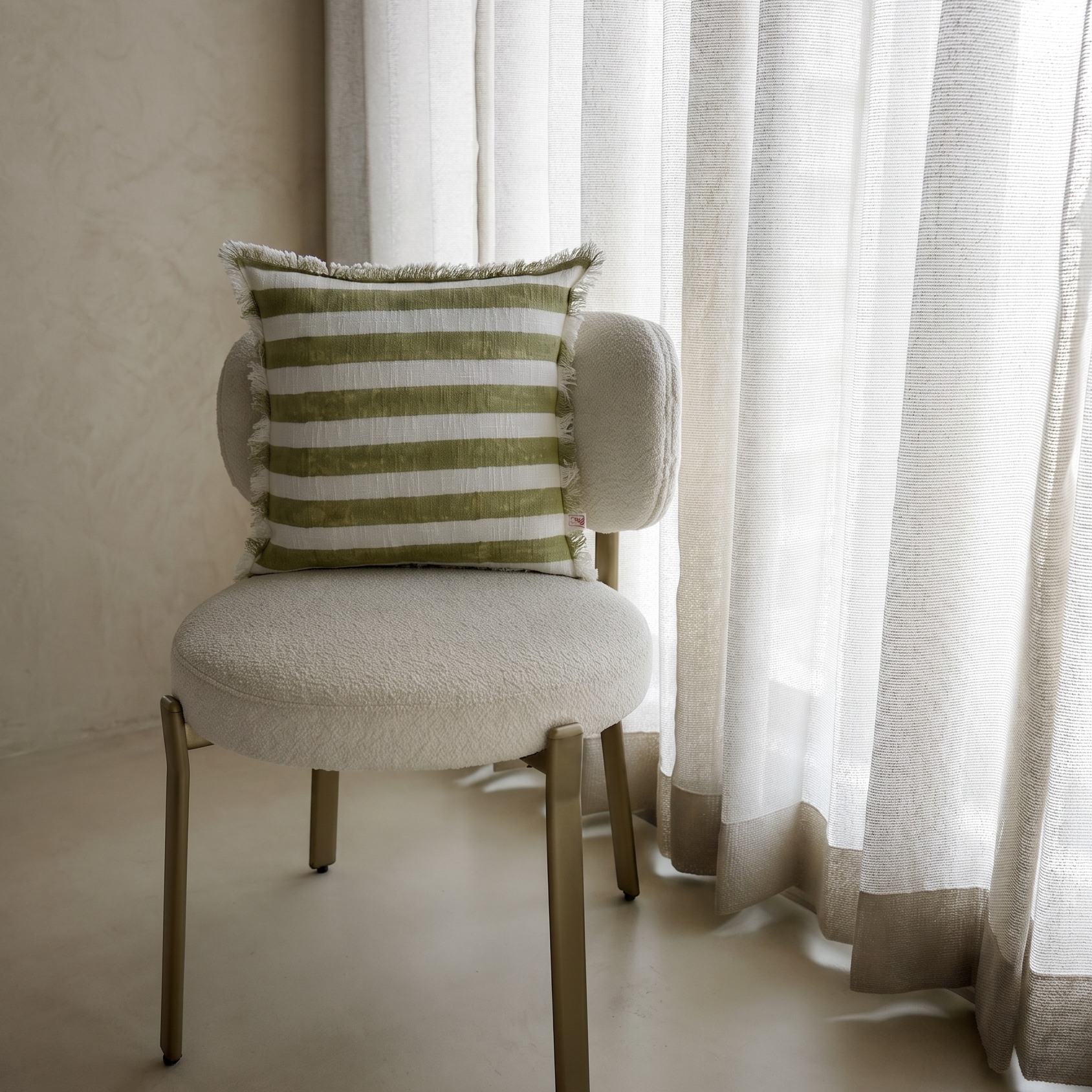 Chair with a striped pillow in front of sheer curtains