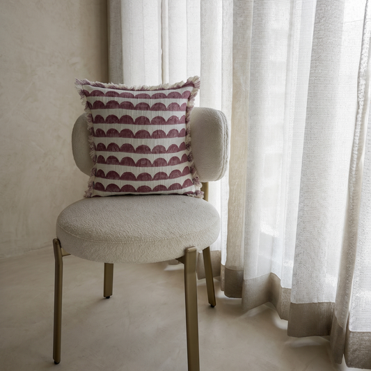 Chair with a patterned pillow in front of sheer curtains