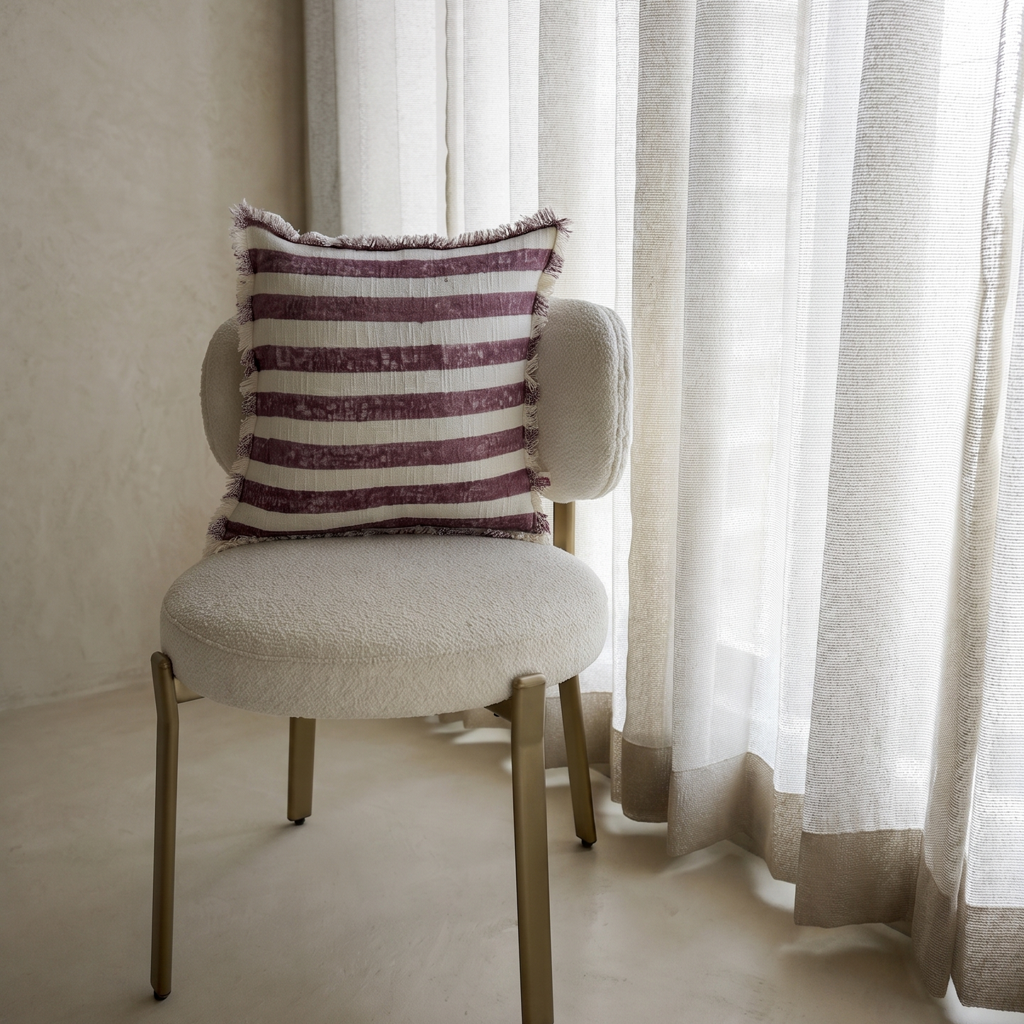 Chair with a striped pillow in front of sheer curtains