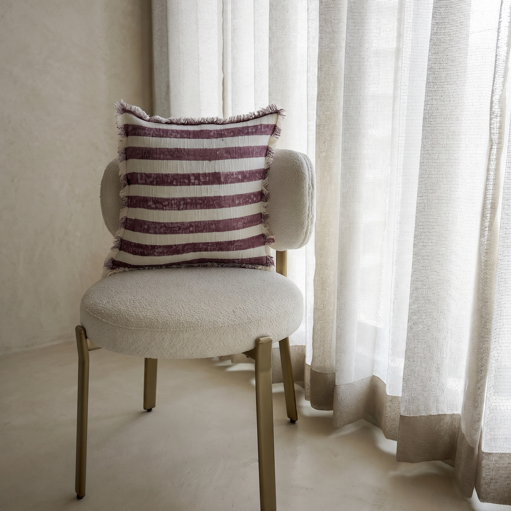Chair with a striped pillow in front of sheer curtains