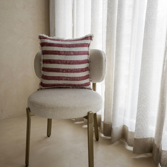 Chair with a striped pillow in front of sheer curtains